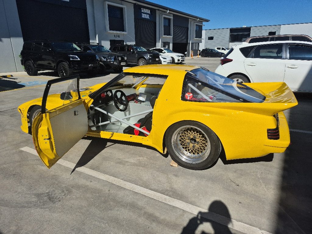 Completed RX-7 race car with rear wing in fresh yellow paint outside MRP Automotive Redland Bay