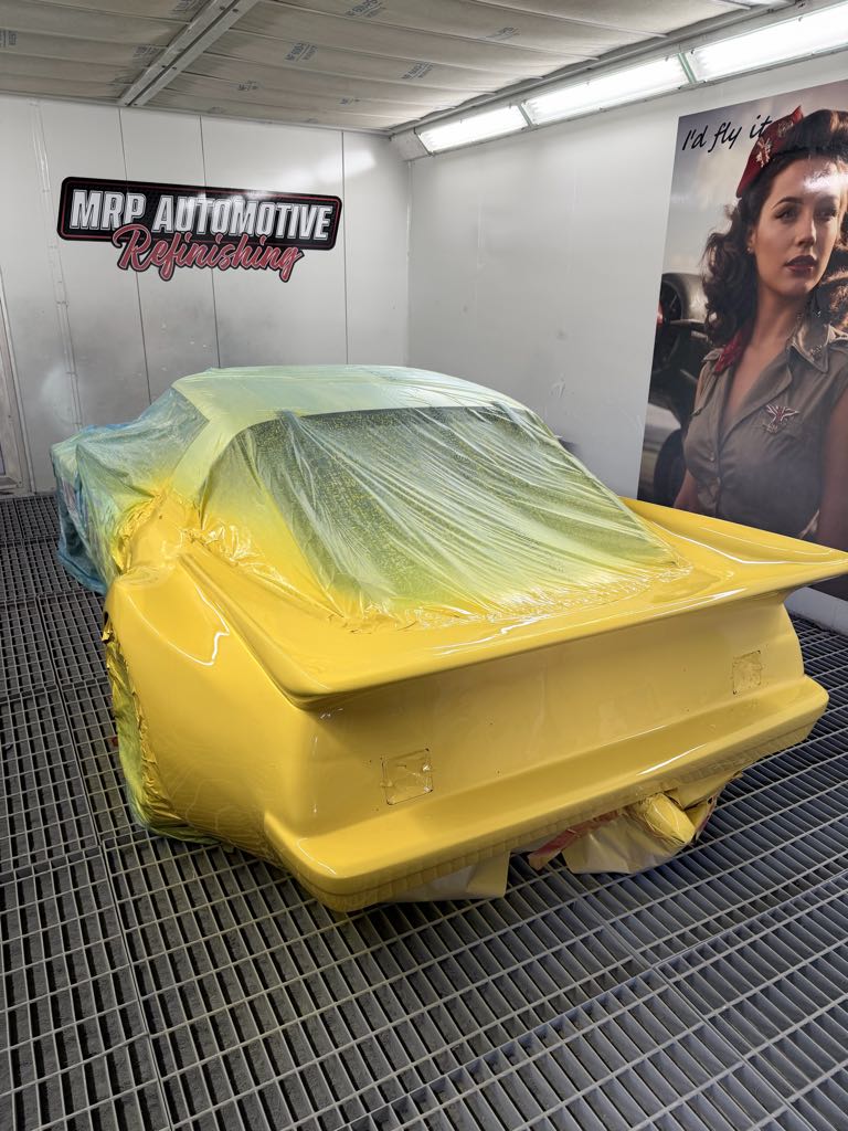 Fresh yellow paint on a masked RX-7 race car in the MRP Automotive downdraft spray booth